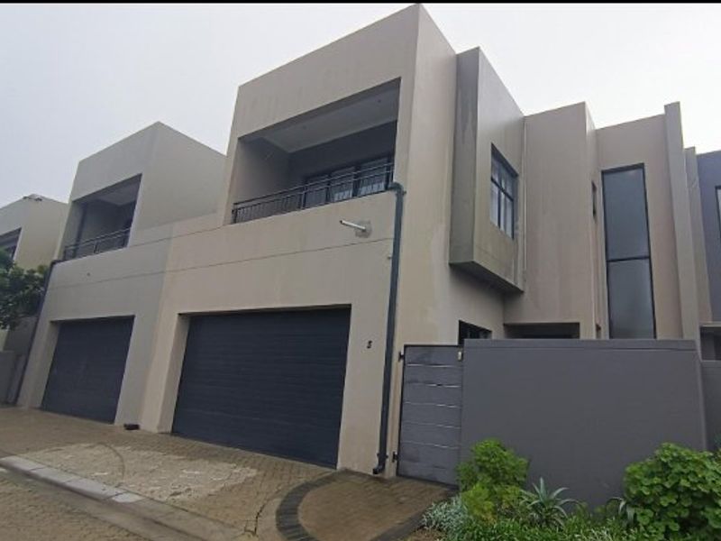 Modern double-storey townhouse facade featuring a double garage, upper-level balcony, and paved driveway entrance.