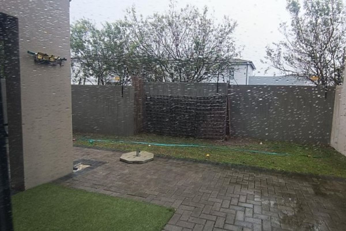 A rear courtyard featuring a paved patio area, boundary wall with trellis, and a small section of artificial grass.