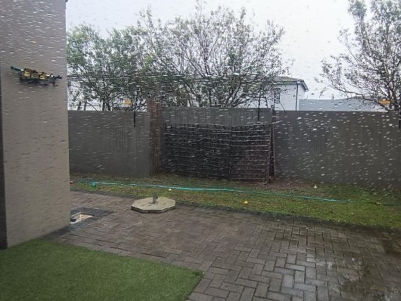 A rear courtyard featuring a paved patio area, boundary wall with trellis, and a small section of artificial grass.
