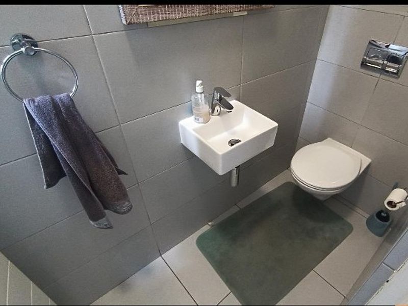 A modern, compact guest bathroom featuring a wall-mounted basin, wall-hung toilet, and neutral grey floor-to-ceiling tiling.