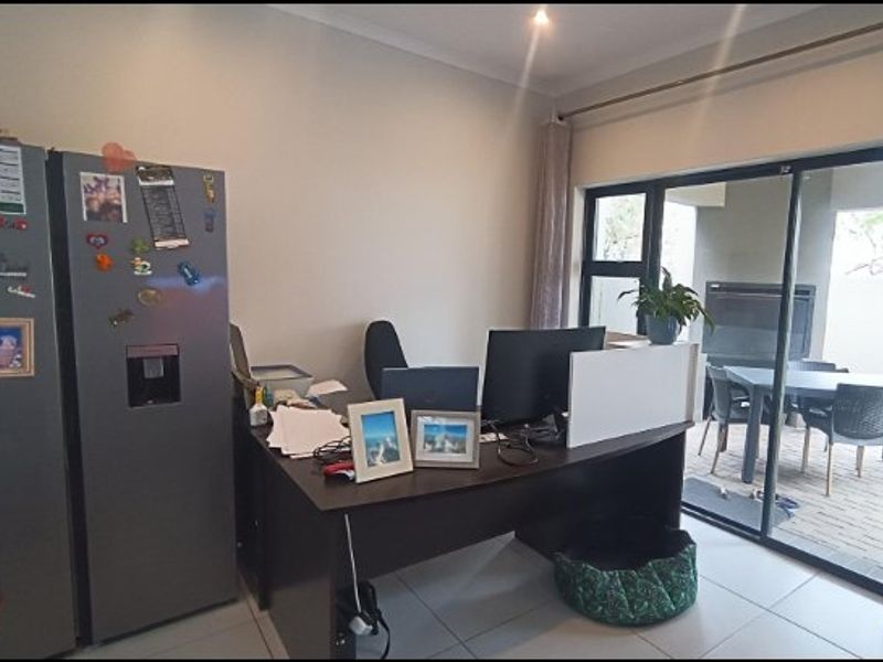 A functional office space featuring tiled flooring and large sliding glass doors that provide direct access to an outdoor patio area.