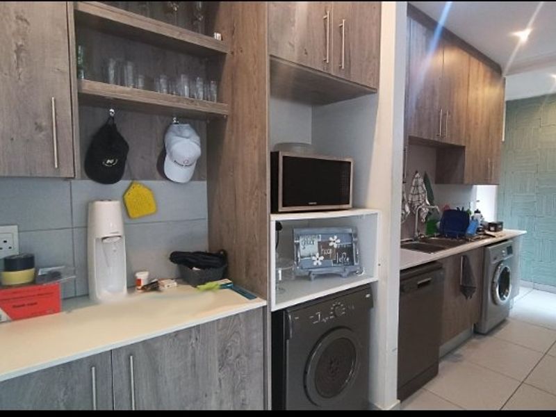 A functional scullery area featuring wood-look cabinetry, tiled flooring, and integrated space for laundry appliances and kitchen prep.