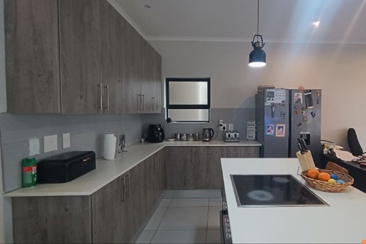 Modern kitchen featuring wood-grain cabinetry, stone countertops, a central island with a built-in hob, and tiled flooring.