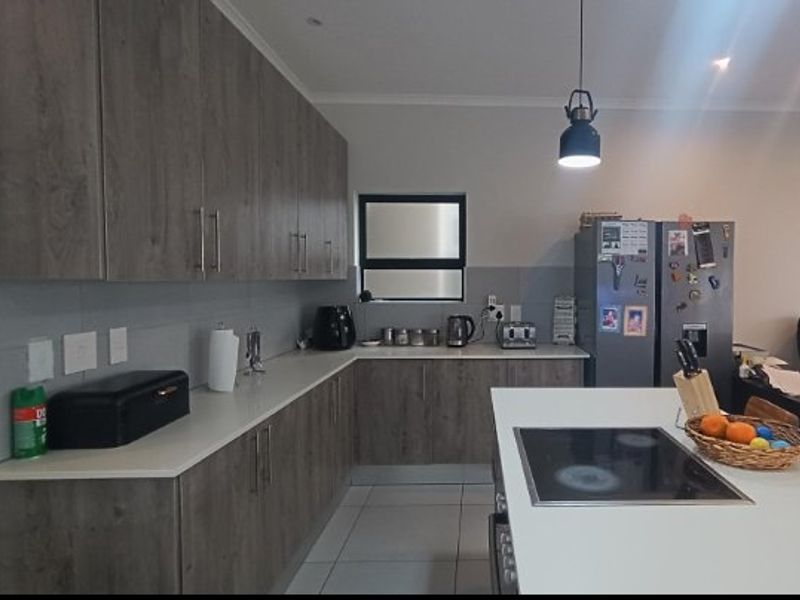 Modern kitchen featuring wood-grain cabinetry, stone countertops, a central island with a built-in hob, and tiled flooring.