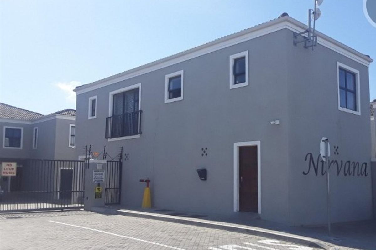 Front exterior view of the apartment complex featuring a paved driveway, secure gated entrance, and grey facade with balcony access.