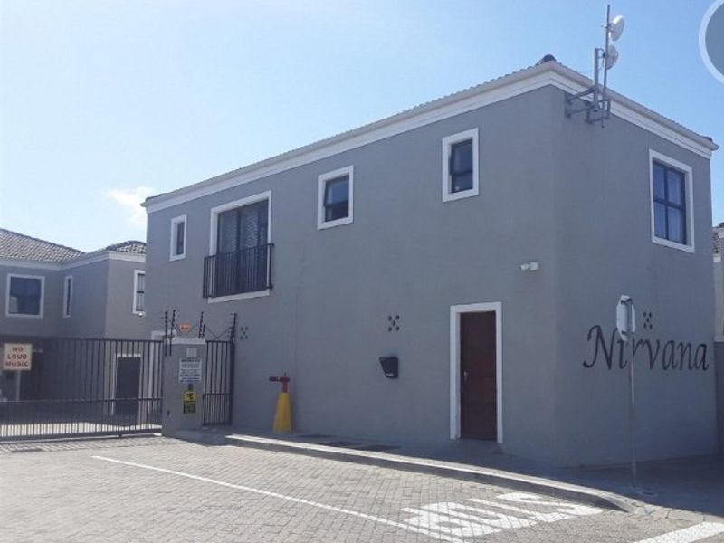 Front exterior view of the apartment complex featuring a paved driveway, secure gated entrance, and grey facade with balcony access.