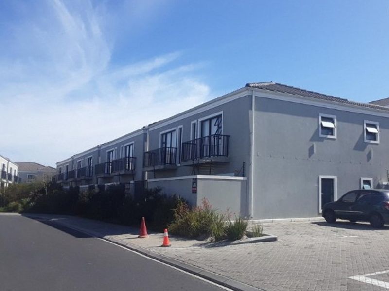 Exterior view of a multi-unit apartment complex featuring a paved driveway, balconies, and perimeter wall with electric fencing.