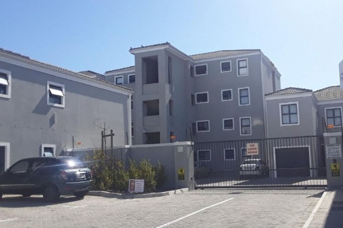 Front exterior view of a multi-story apartment complex featuring paved parking, secure gated access, and perimeter electric fencing.