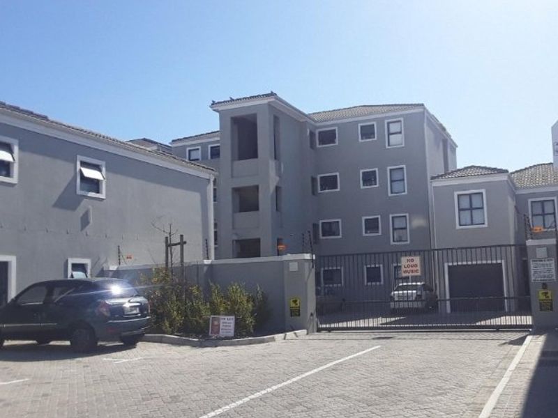 Front exterior view of a multi-story apartment complex featuring paved parking, secure gated access, and perimeter electric fencing.