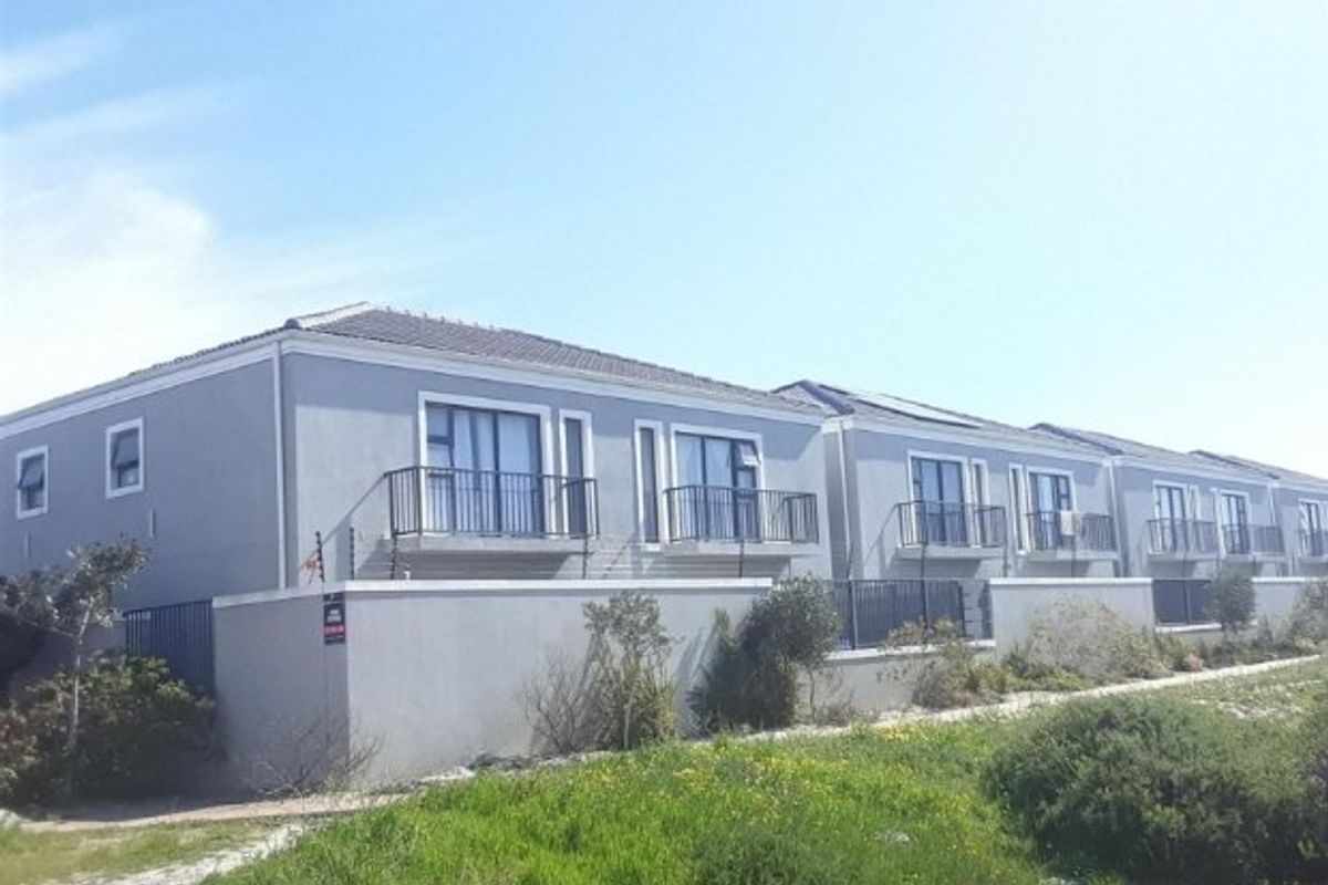 Exterior view of a multi-unit apartment complex featuring grey rendered facades, tiled roofing, and private balconies with metal railings.