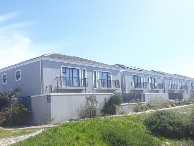 Exterior view of a multi-unit apartment complex featuring grey rendered facades, tiled roofing, and private balconies with metal railings.