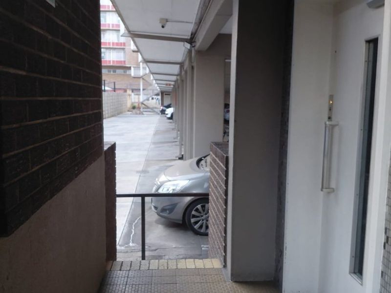 A covered exterior walkway leading to a building entrance, featuring brick walls, concrete pillars, and tiled flooring.