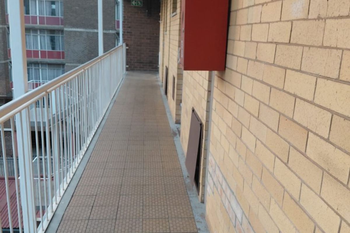 An exterior apartment building walkway featuring brick walls, tiled flooring, and a metal safety balustrade.