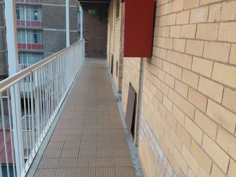 An exterior apartment building walkway featuring brick walls, tiled flooring, and a metal safety balustrade.