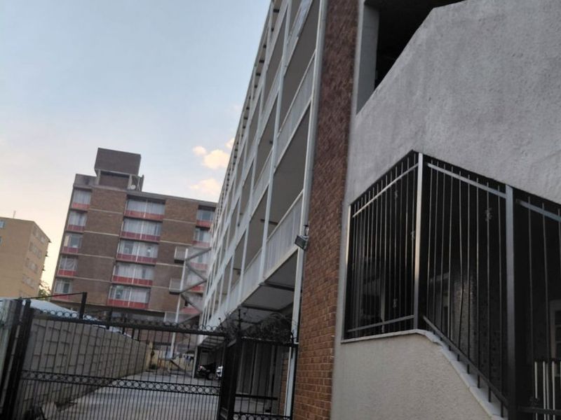 Exterior view of an apartment building complex featuring a secure gated entrance, concrete driveway, and fire hydrant infrastructure.