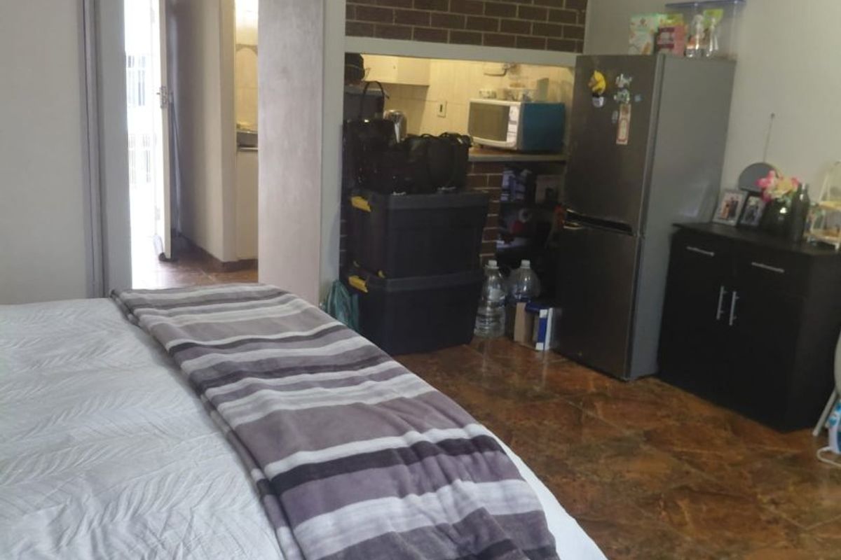 Bedroom featuring tiled flooring and an exposed brick feature wall, with an adjacent hallway leading to other areas of the apartment.
