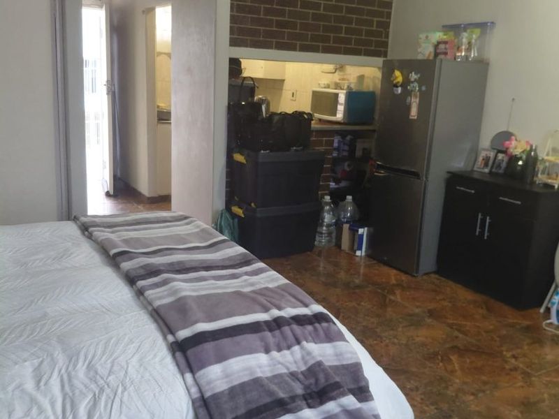 Bedroom featuring tiled flooring and an exposed brick feature wall, with an adjacent hallway leading to other areas of the apartment.