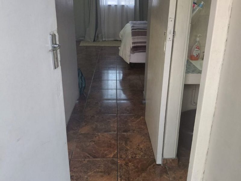 A view through a hallway with tiled flooring leading towards a bedroom and a small bathroom area.