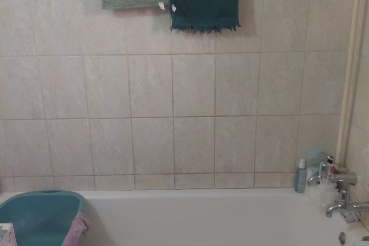 A bathroom featuring a standard bathtub with tiled wall surround and a tiled apron, showing signs of wear and dated finishes.
