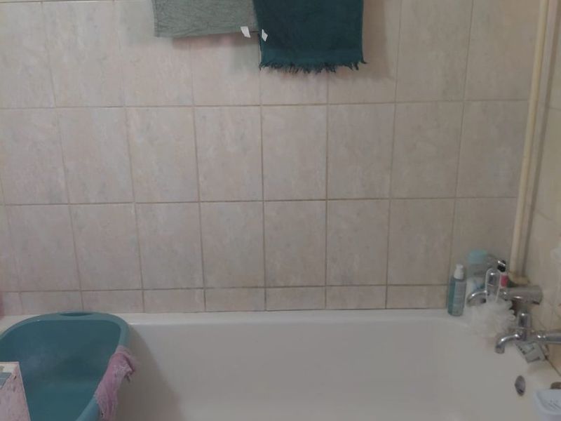 A bathroom featuring a standard bathtub with tiled wall surround and a tiled apron, showing signs of wear and dated finishes.