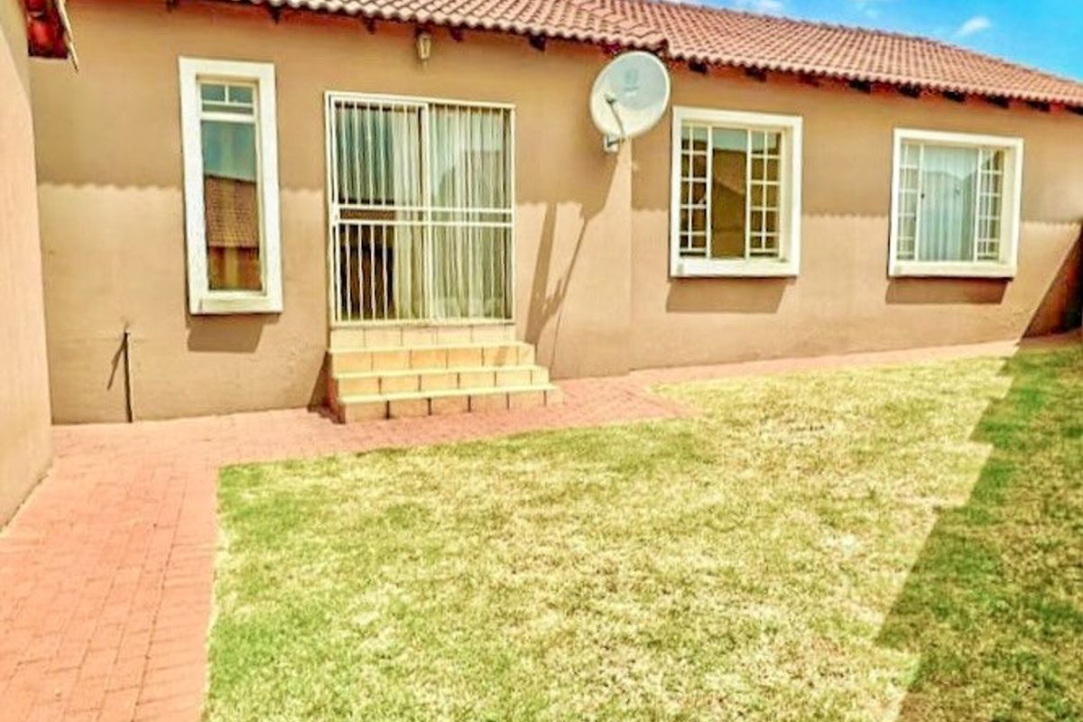 Rear view of the house featuring a tiled roof, sliding door access with security gate, brick paved walkway, and a well-maintained lawn.