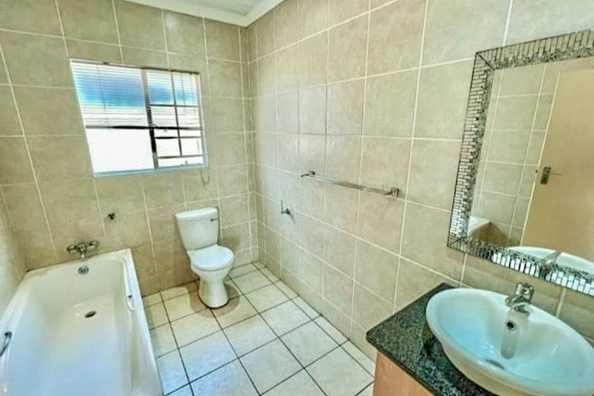 A functional bathroom featuring full-height wall tiling, a bathtub, a toilet, and a vanity basin with a granite countertop.