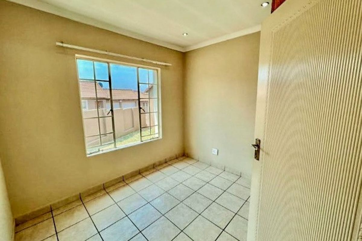 A clean, empty bedroom featuring neutral wall tones, tiled flooring, and recessed downlighting, providing a versatile space ready for personalization.