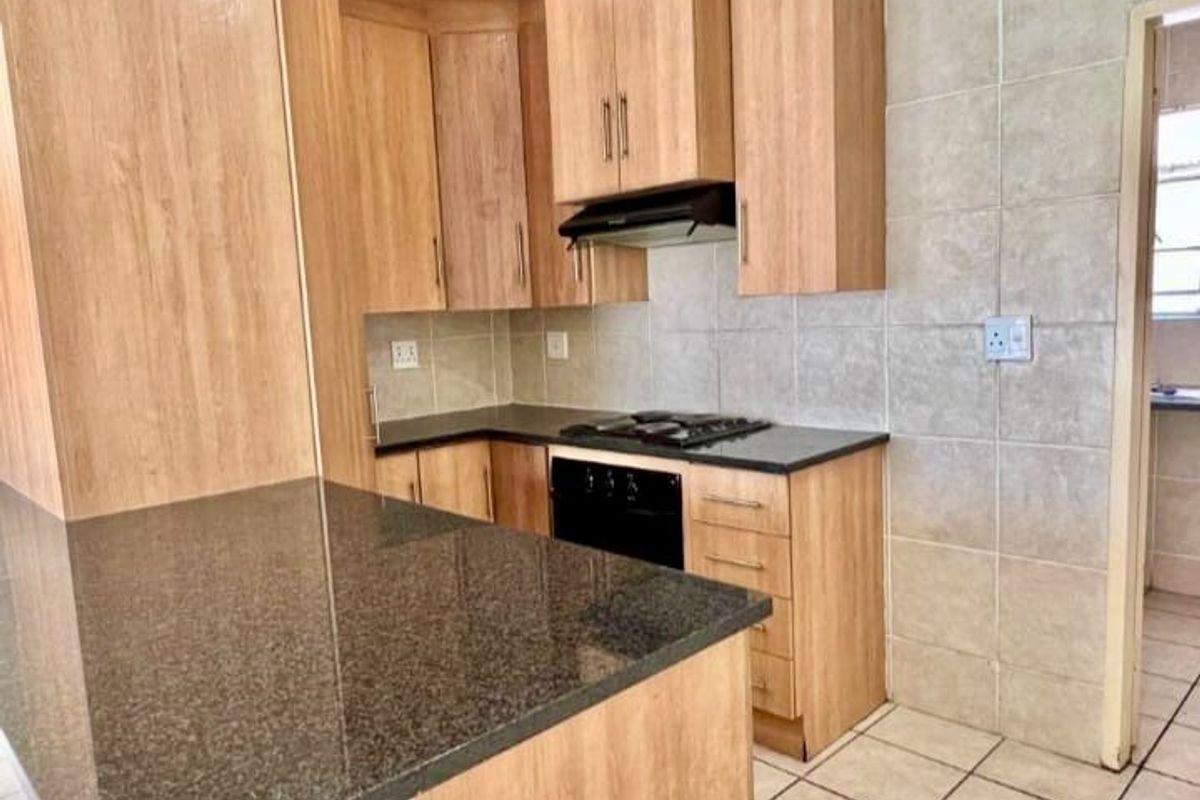 A functional kitchen featuring light wood-finish cabinetry, dark granite countertops, a built-in oven, gas hob, and neutral tiled splashbacks.