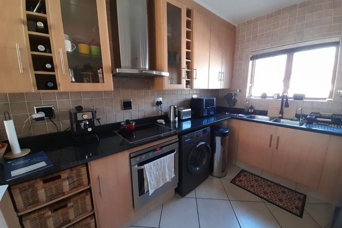 Functional kitchen featuring light wood cabinetry, granite countertops, integrated oven and hob, stainless steel extractor, and tiled finishes throughout.
