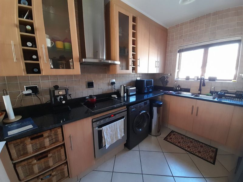 Functional kitchen featuring light wood cabinetry, granite countertops, integrated oven and hob, stainless steel extractor, and tiled finishes throughout.