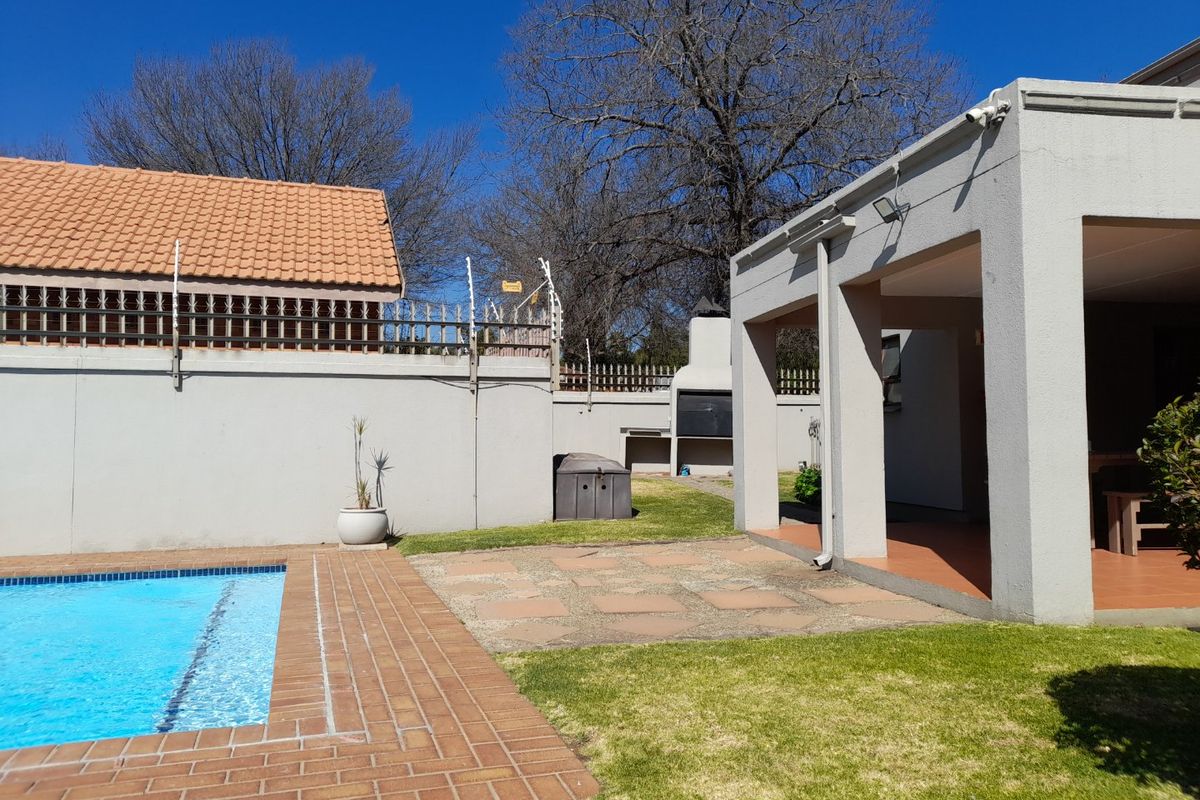 Rear garden area featuring a swimming pool, paved patio, and a covered entertainment space with a built-in braai.