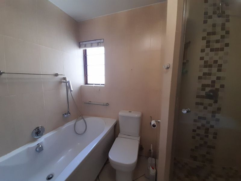 A functional bathroom featuring a bathtub, separate shower enclosure with mosaic tile accents, and a standard toilet.