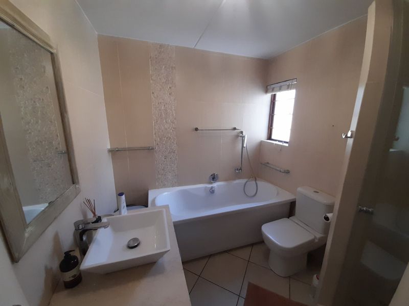 A functional bathroom featuring a vessel sink, built-in bathtub, and toilet with neutral wall and floor tiling.