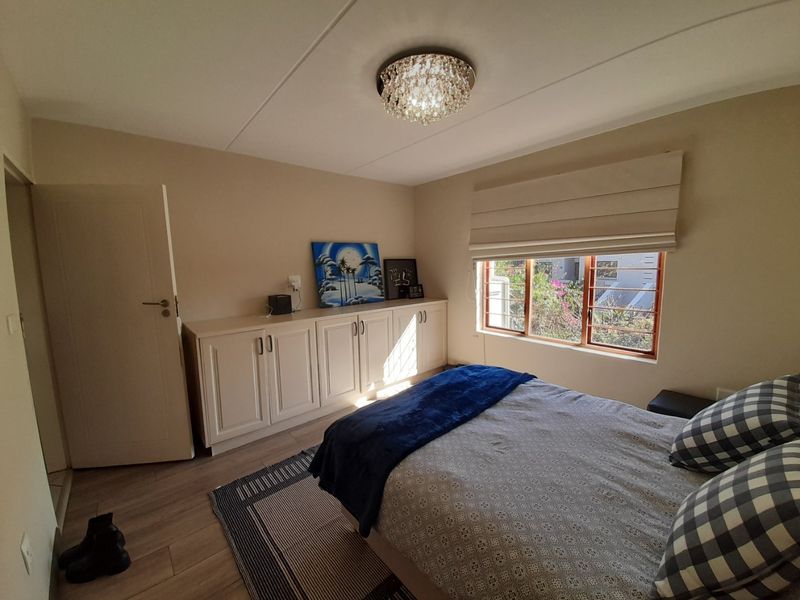 A well-maintained bedroom featuring neutral walls, laminate flooring, built-in storage cabinetry, and a window fitted with security bars and a roman blind.