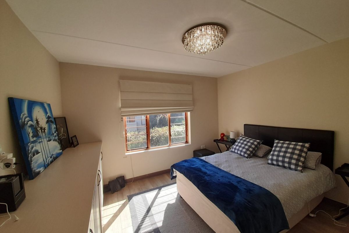 A well-maintained bedroom featuring laminate flooring, built-in cabinetry, and a window with security bars, providing a comfortable and functional living space.