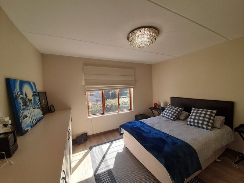 A well-maintained bedroom featuring laminate flooring, built-in cabinetry, and a window with security bars, providing a comfortable and functional living space.