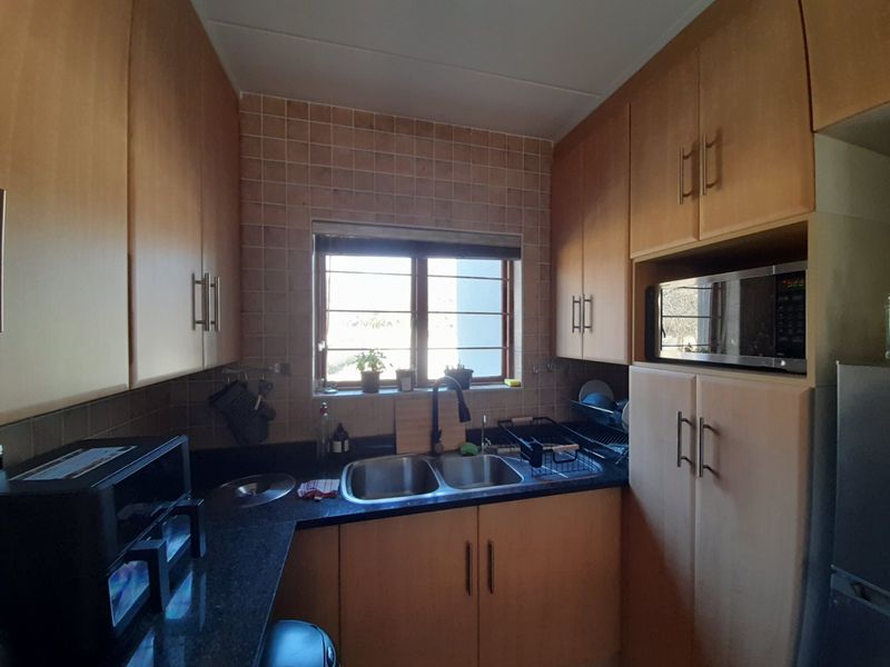 Compact kitchen featuring light wood cabinetry, dark granite countertops, a double basin sink, and a tiled backsplash with a window for natural light.
