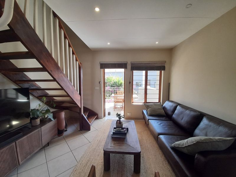 A living room featuring a timber staircase, tiled flooring, and direct access to an outdoor balcony area.