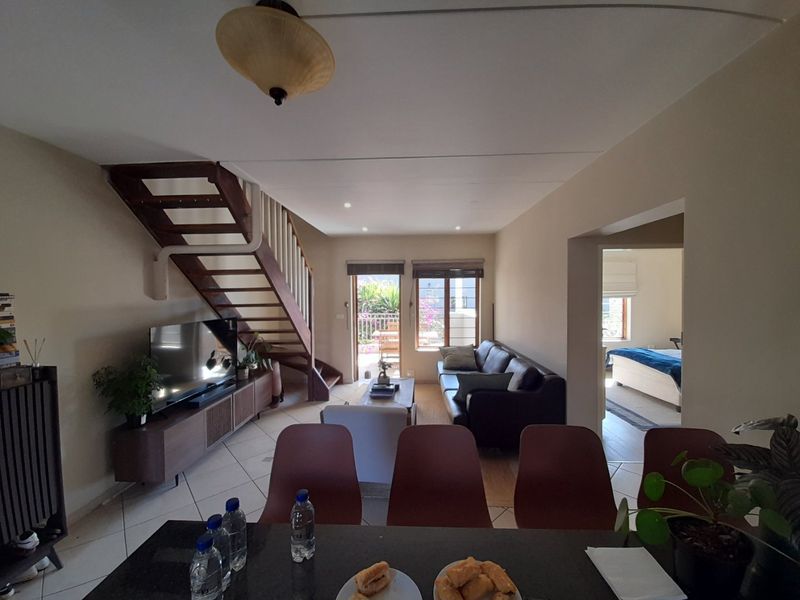 Open-plan living area featuring tiled flooring, a timber staircase, and direct access to an outdoor patio space.