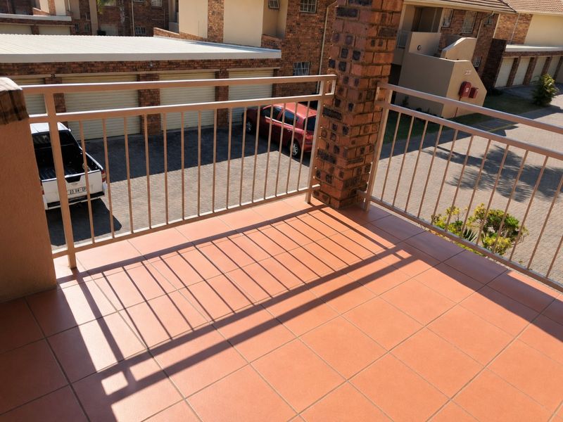 A clean, open-air balcony featuring terracotta tiling and a metal balustrade, overlooking the complex parking area.