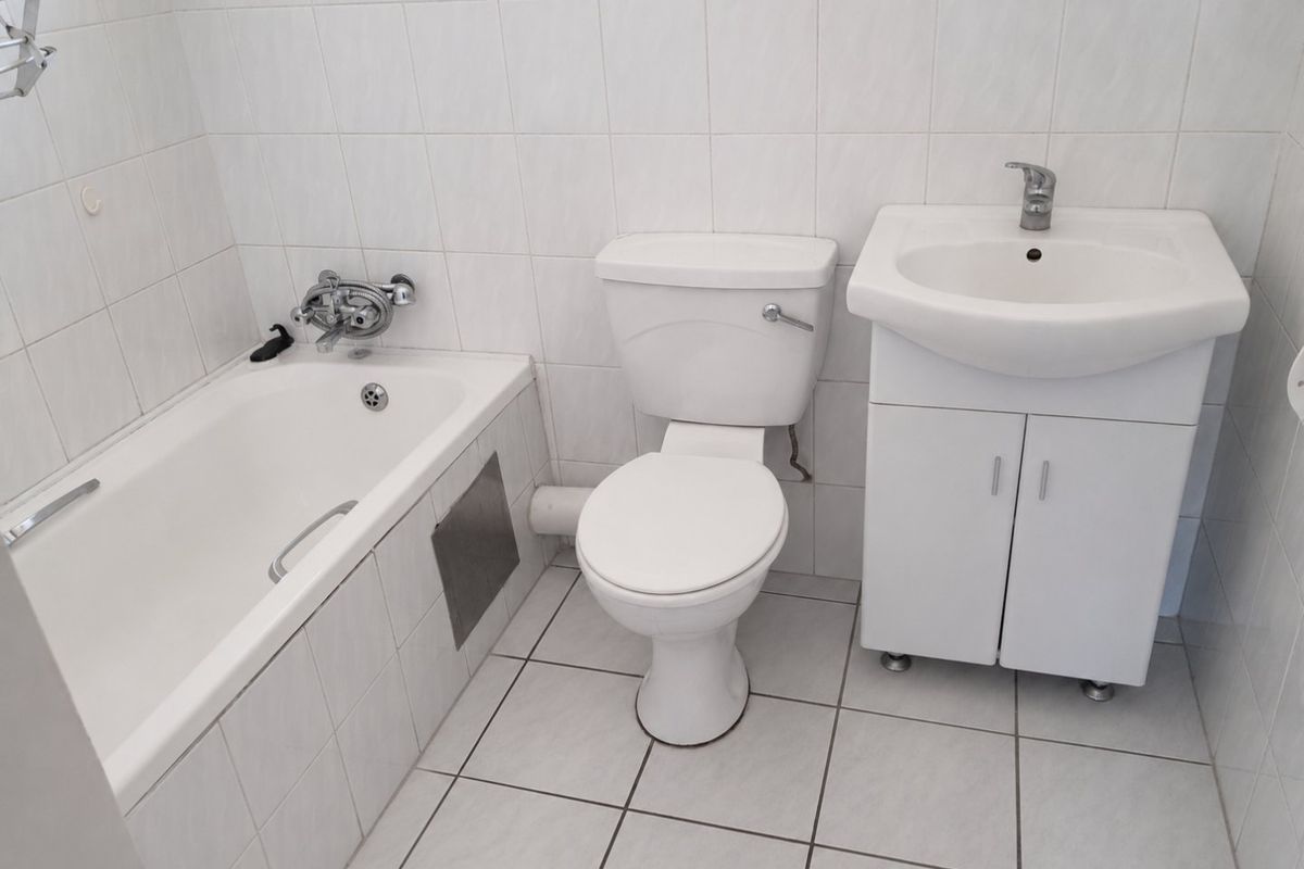 A functional bathroom featuring a white bathtub, toilet, and a vanity cabinet with a washbasin, finished with neutral wall and floor tiles.