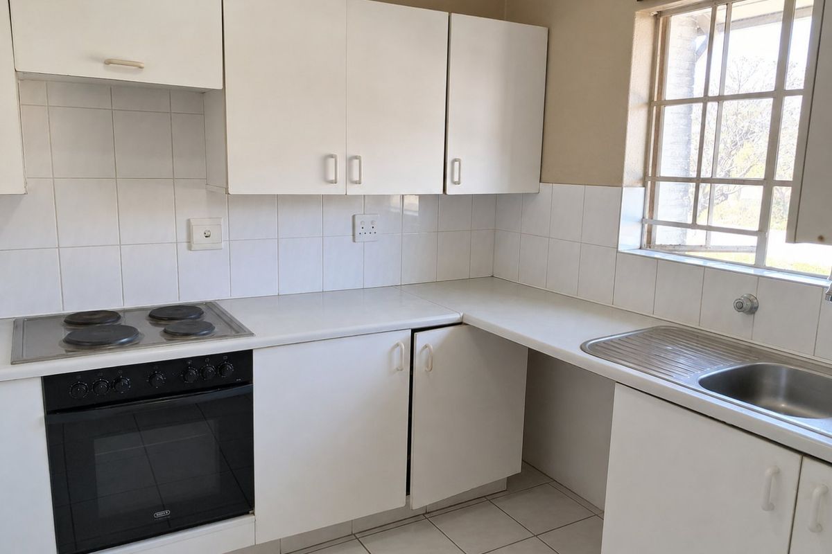A functional kitchen featuring white cabinetry, a built-in oven with electric hob, tiled backsplash, and a stainless steel sink under a window.