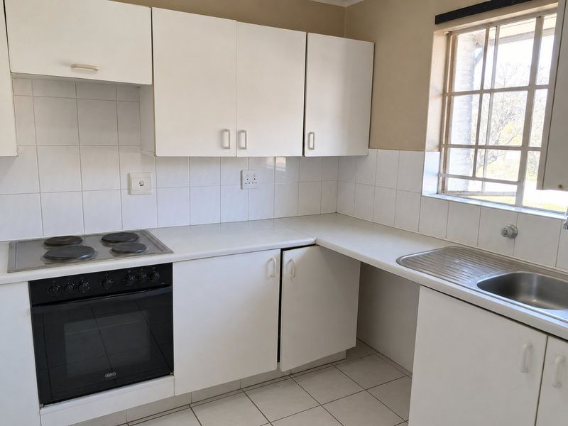A functional kitchen featuring white cabinetry, a built-in oven with electric hob, tiled backsplash, and a stainless steel sink under a window.