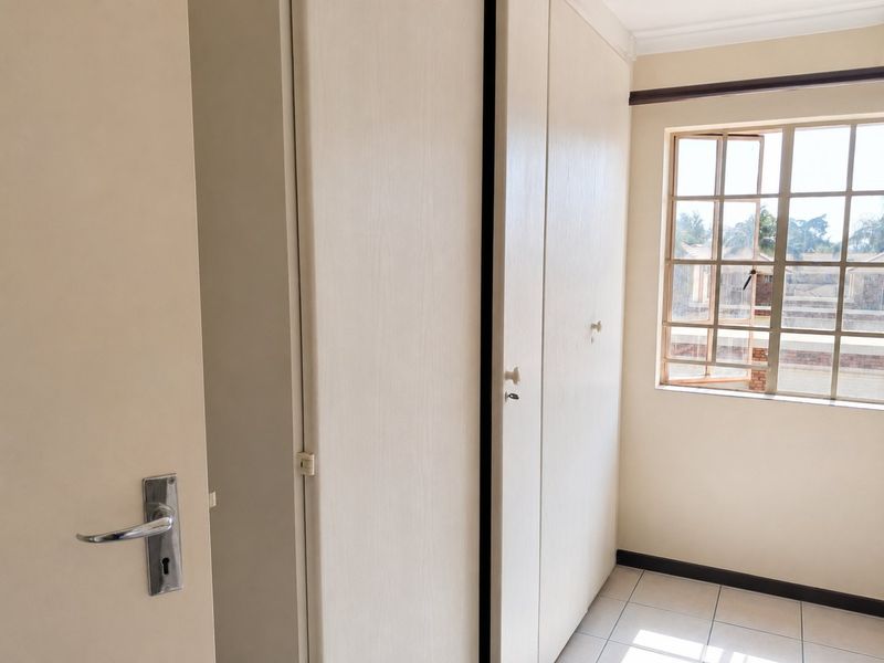 A bright, empty bedroom featuring built-in cupboards, tiled flooring, and a window with security bars.