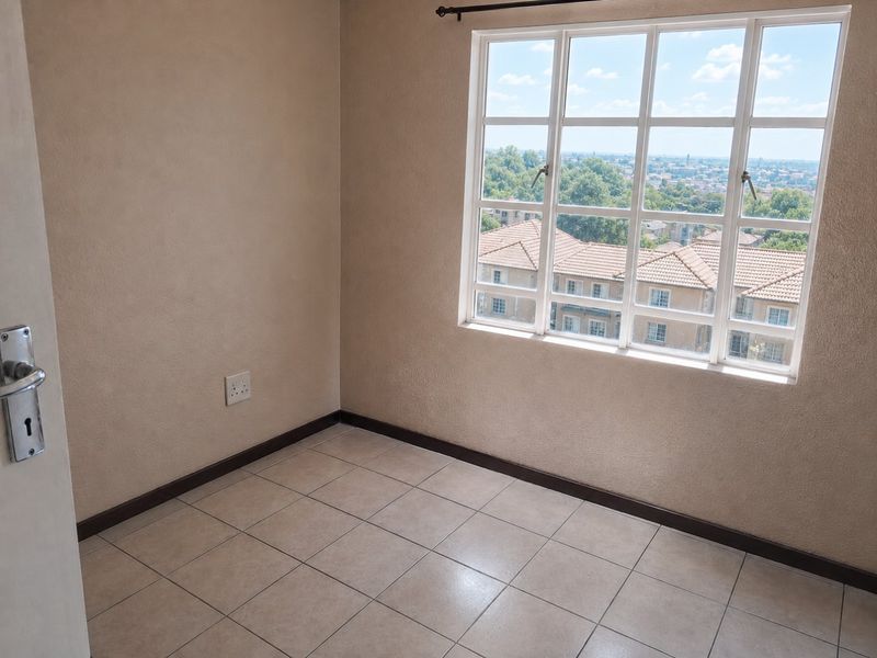 An empty bedroom featuring tiled flooring, a large multi-pane window with exterior views, and neutral wall finishes.