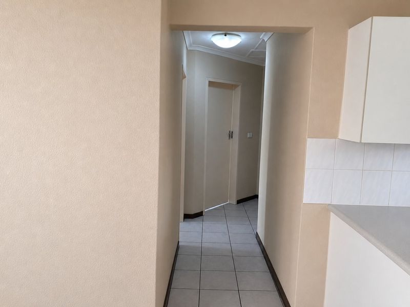 A clean, neutral-toned hallway featuring tiled flooring and access to internal rooms, providing a functional transition space within the apartment.