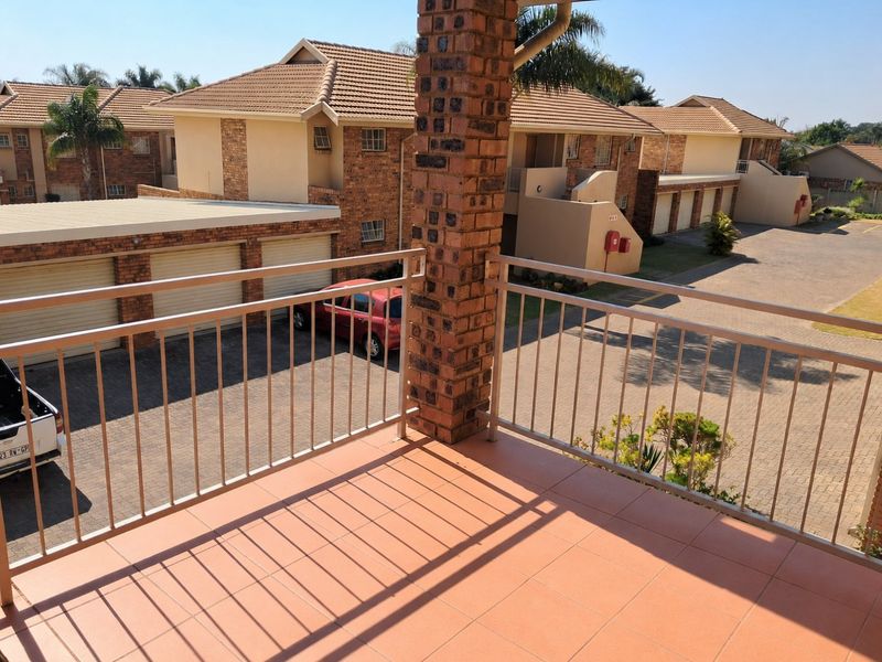 A private balcony featuring tiled flooring, a sturdy brick support pillar, and a metal balustrade, overlooking the apartment complex parking area.
