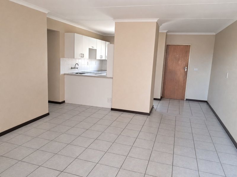 An open-plan living and kitchen area featuring neutral wall tones, tiled flooring, and functional kitchen cabinetry in a clean, vacant apartment setting.