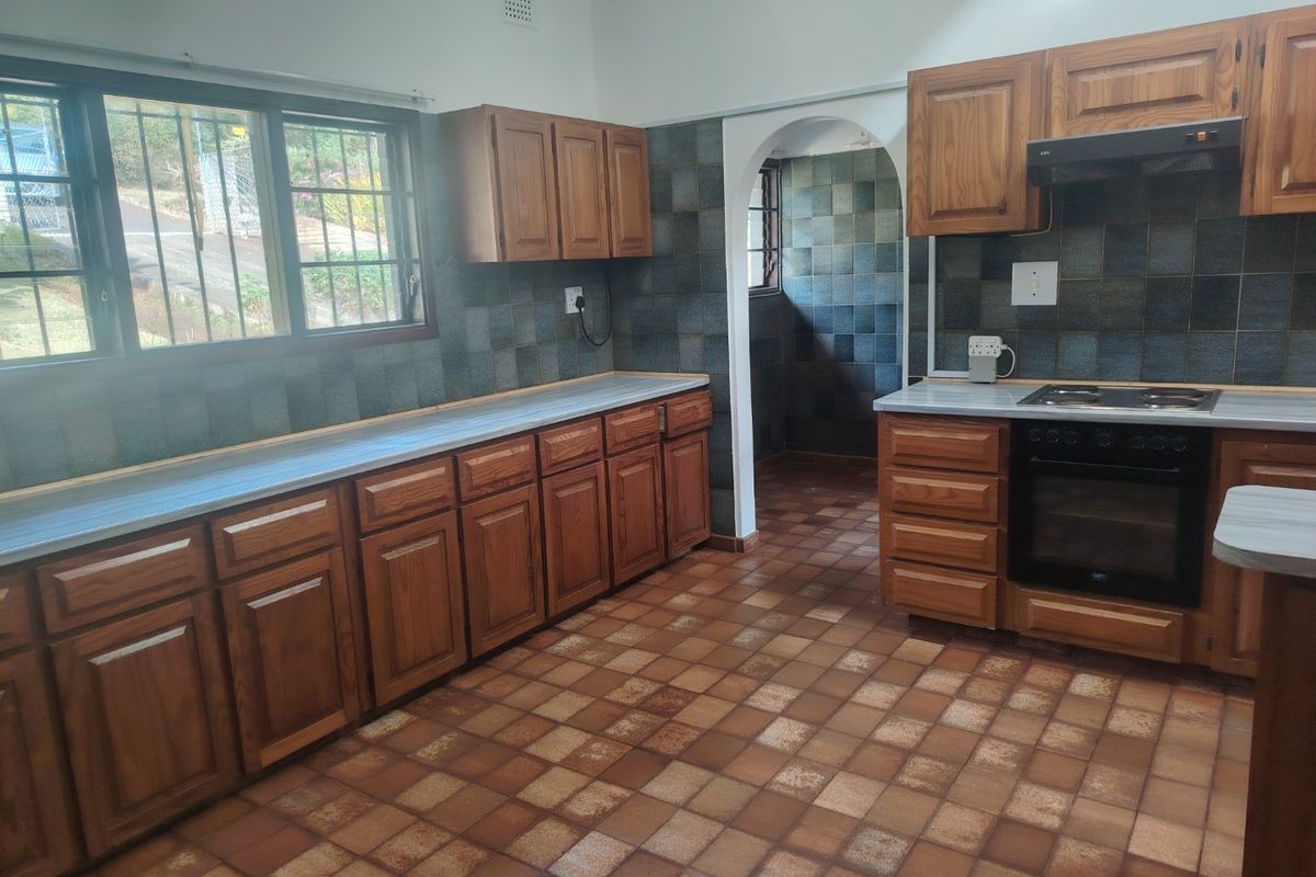 A functional kitchen featuring wooden cabinetry, built-in oven and hob, tiled splashbacks, and tiled flooring, offering a classic layout ready for modernization.