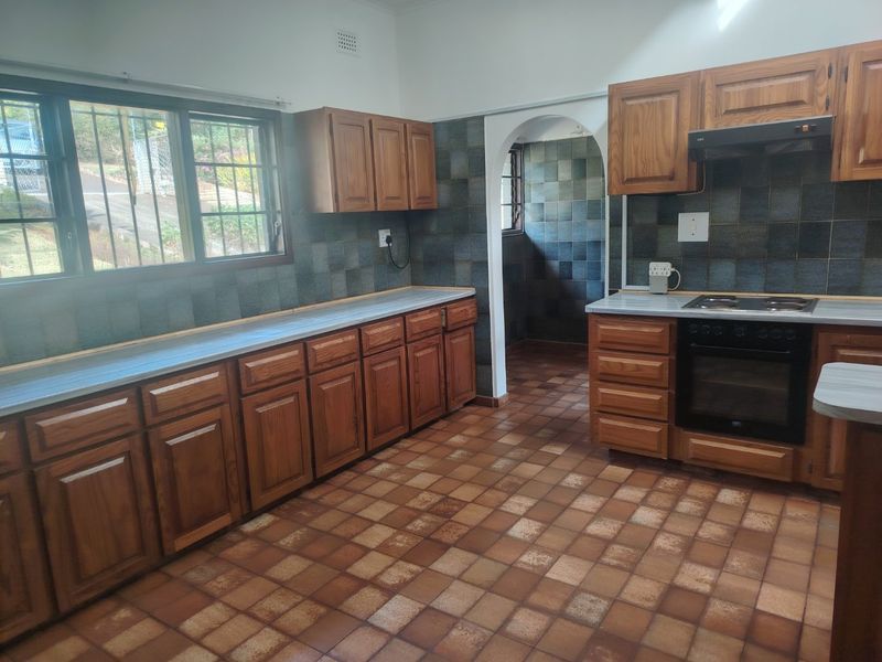 A functional kitchen featuring wooden cabinetry, built-in oven and hob, tiled splashbacks, and tiled flooring, offering a classic layout ready for modernization.